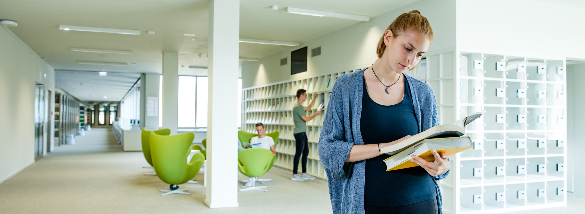 Studierende in der Bereichsbibliothek Westerberg, im Hintergrund: grüne Sitzgruppe mit Egg und Swan Chairs von Arne Jacobsen, Foto: Simone Reukauf
